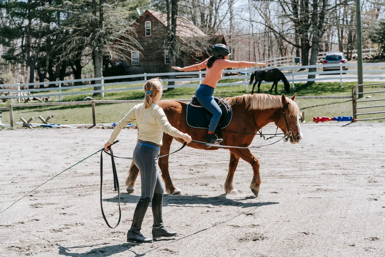 A young student learns horseback riding under the guidance of an instructor outdoors.